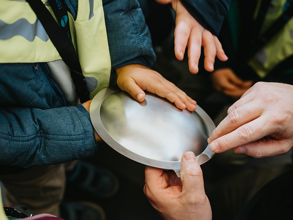 Rembe3 Kinderhände und eine Erwachsenenhand fassen eine Metallscheibe an.