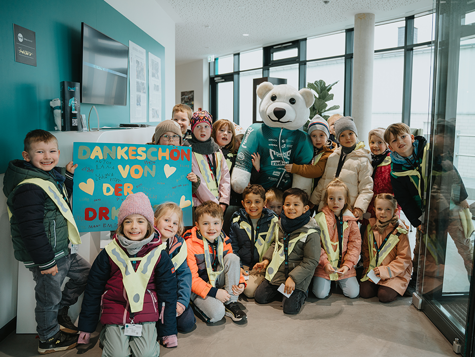Rembe4 Die Kinder stehen in einer Gruppe und schauen in die Kamera. Sie haben Jacken und Mützen an und tragen Warnwesten. In der Mitte steht das Makottchen der Firma Rembe, ein Eisbär.