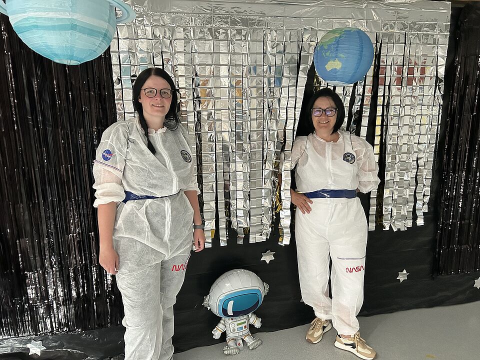 Zwei Astronautinnen mit kleinem Roboter zwischen Planeten