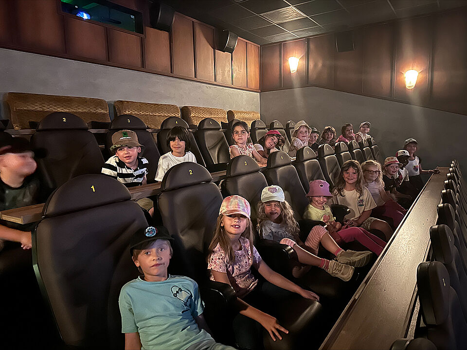 Die Vorschulkinder sitzen in zwei Sitzreihen im Kino und warten darauf, dass der Film losgeht. 