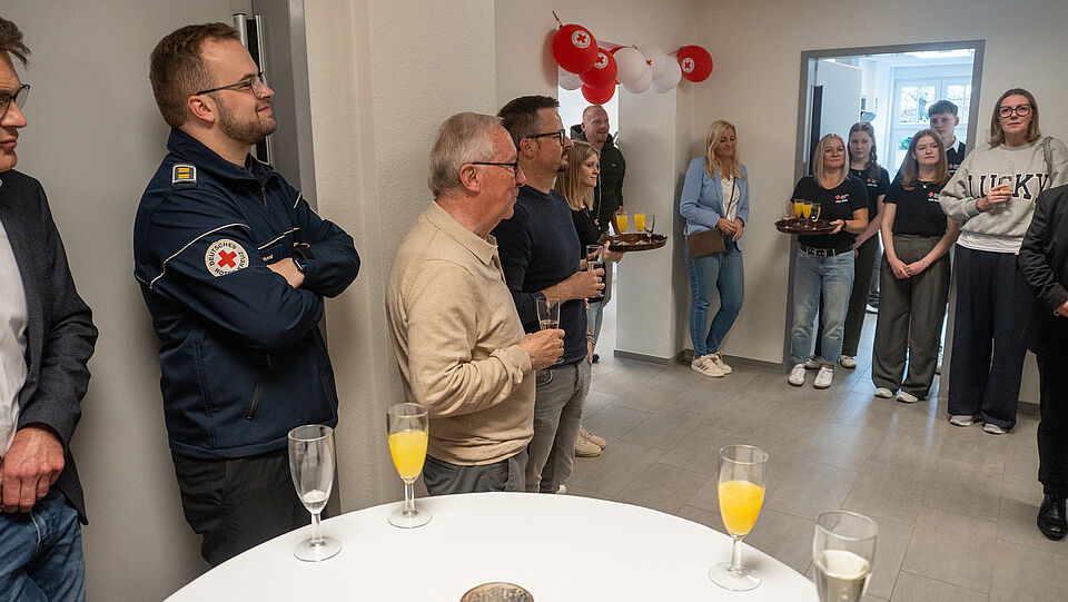 Rotkreuzleitung Niklas Berhorst, Präsident Reinhard Sommer und Prokurist Thorsten Rediger hören bei der Rede von Julia Drewes zu. Im Hintergrund stehen weitere Gäste.