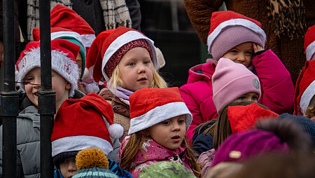 Kinder singen Weihnachtslieder und tragen dabei Weihnachtsmützen.
