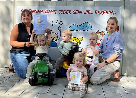 Frau Drewes und Frau Runte freuen sich mit den Kindern über die Zertifizierung und halten diese in der Hand.