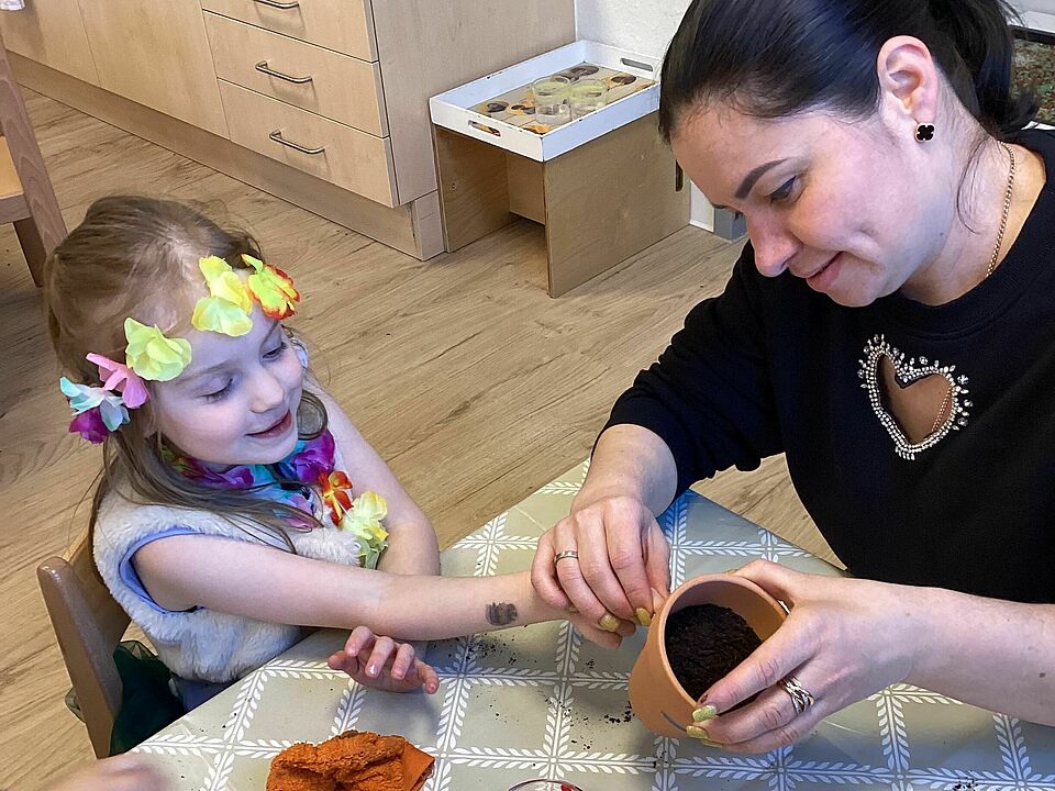 Mutter und die ca. 4-jährige Tochter betupfen gemeinsam einen Tontopf mit Farbe.