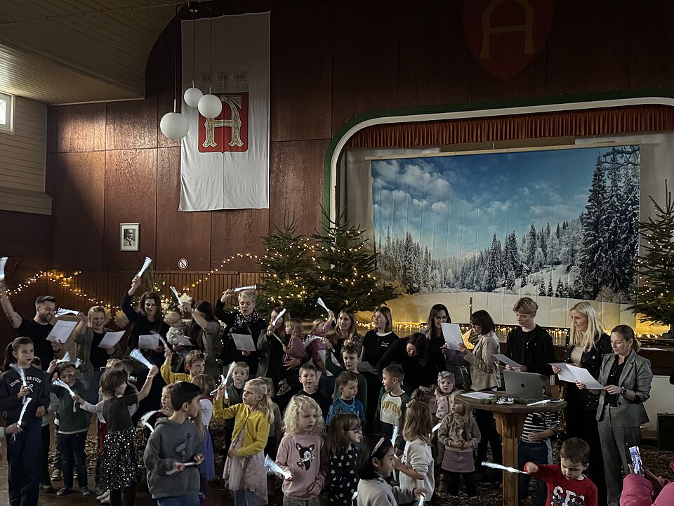 IMG 8365 Kinder die vor der Bühne stehen und etwas singen. Das Bühnenbild und die Schützenhalle sind weihnachtlich eingerichtet.