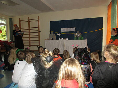 Passend zum Halloween verkleidete Kinder, die einer Erzieherin beim Geschichte vorlesen zu hören und ein Bühnenbild dabei anschauen. 