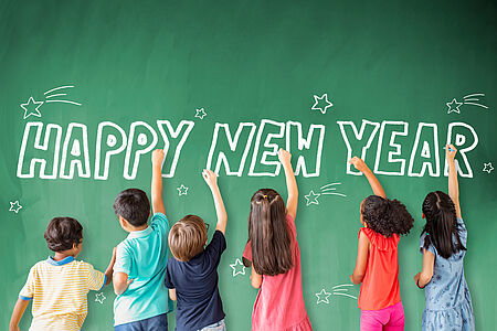 Kinder schreiben "Happy New Year" an eine Tafel