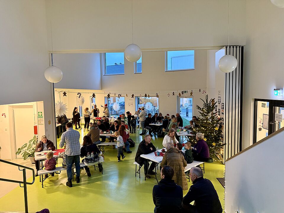6881 Ein Blick auf das Foyer und die Turnhalle. Viele Menschen sitzen an den Tischen zusammen und genießen die Leckereien vom Kita Team
