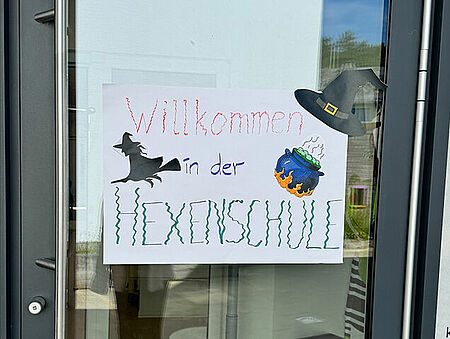 An der Tür der Kita hängt ein Schild, auf dem steht: Willkommen in der Hexenschule.