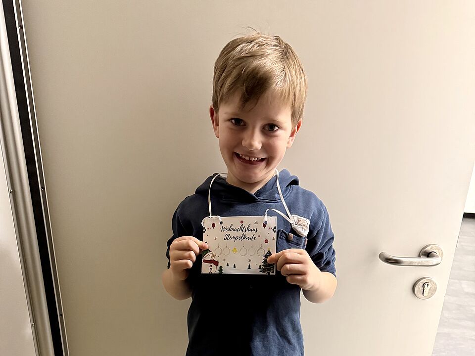 6863 Ein Junge lächelt in die Kamera und zeigt stolz seine selbstgebastelte Karte