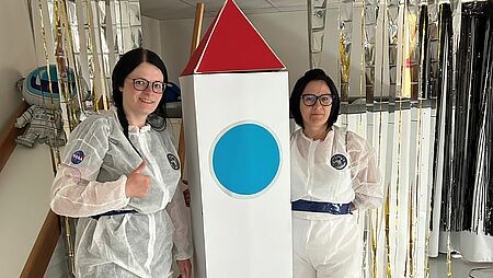 zwei Erzieherinnen als Astronautinnen verkleidet mit einer Rakete zeigen den Daumen hoch