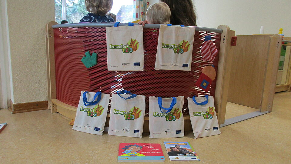 Büchertaschen sind an einer Sitzecke aufgestellt. In der Sitzecke sitzen Kinder von der Kamera weggedreht. 
