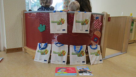 Büchertaschen sind an einer Sitzecke aufgestellt. In der Sitzecke sitzen Kinder von der Kamera weggedreht. 