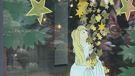 Auf dem Bild sieht man das Adventsfenster, mit einem Christkind, das in die Sterne schaut in mitten eines Waldes