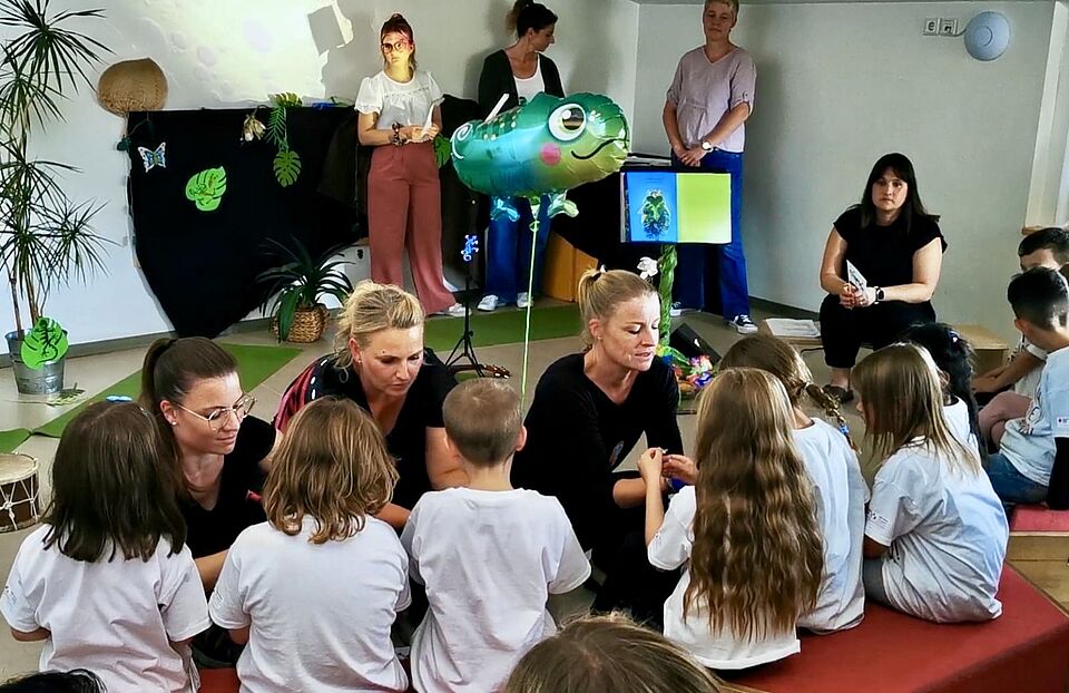 Die Vorschulkinder sitzen in einer Reihe vor ihren Erzieherinnen, die ihnen ein Armband umlegen zur Erinnerung an die Kitazeit.