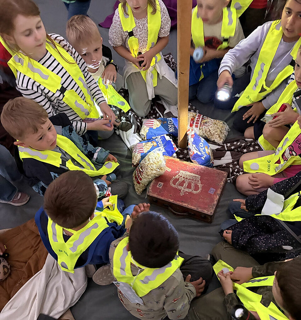 Die Vorschulkinder sitzen im Indianerzelt um ihren Schatz, der aus Popcorn besteht, und haben dabei Warnwesten an.