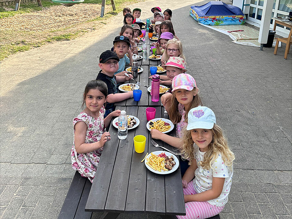 Die Vorschulkinder essen Pommes und Wurst auf dem Außengelände der Kita an einer langen Tafel