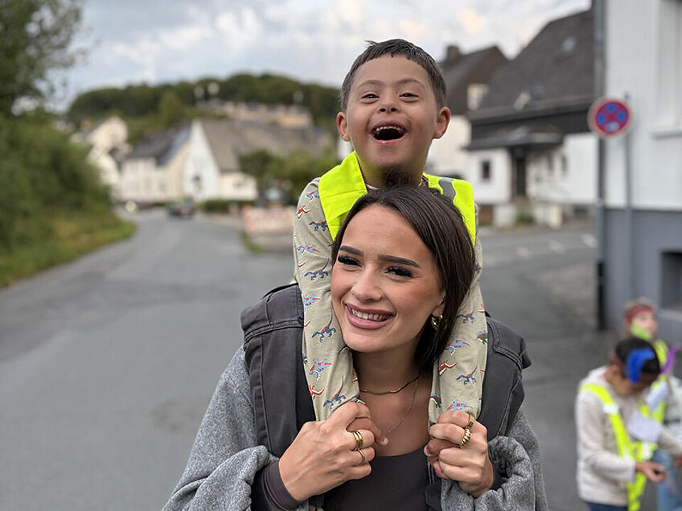 Eine Erzieherin trägt ein Vorschulkind auf ihren Schultern, beide lachen dabei in die Kamera