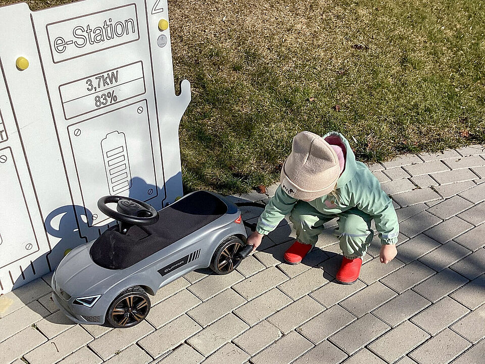 Ein Kind hockt neben dem Ruschauto und betankt es an der Spielzeugtankstelle. 