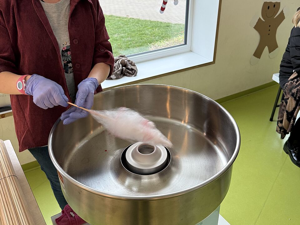 6869 Eine Mitarbeiterin dreht einen Spieß in einer Wanne und stellt Zuckerwatte her.